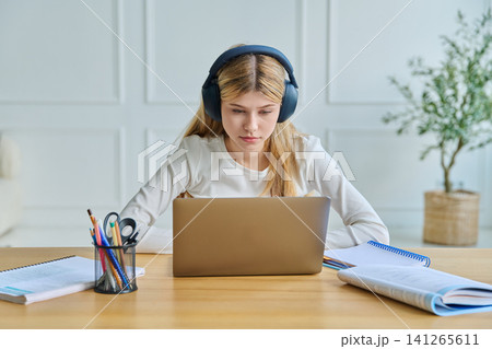 Focused teenage girl in headphones studying with laptop Focused teenage girl in headphones studying with laptop 141265611