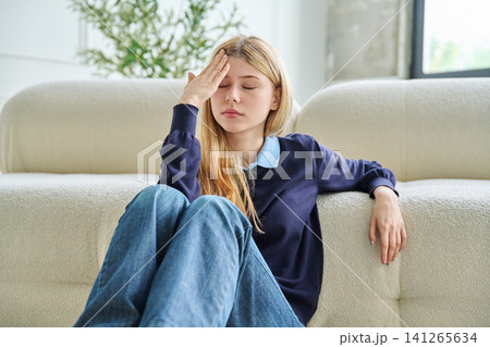 Tired teenage student girl with headache sitting on floor holding forehead. 141265634