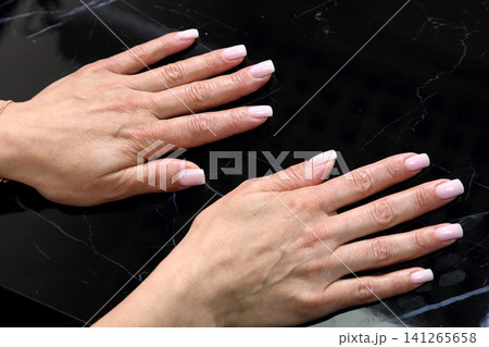 Receiving Professional Manicure in Modern Salon. Beautiful, well-groomed women's hands with elegant nails against a dark background. Beauty salon concept: manicures, pedicures. Receiving Professional Manicure in Modern Salon. Beautiful, well-groomed women's hands with elegant nails against a dark background. Beauty salon concept: manicures, pedicures. 141265658
