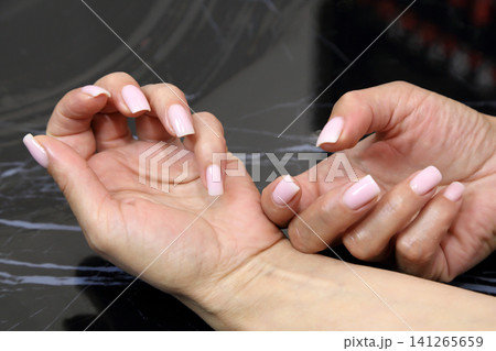 Receiving Professional Manicure in Modern Salon. Beautiful, well-groomed women's hands with elegant nails against a dark background. Beauty salon concept: manicures, pedicures. 141265659