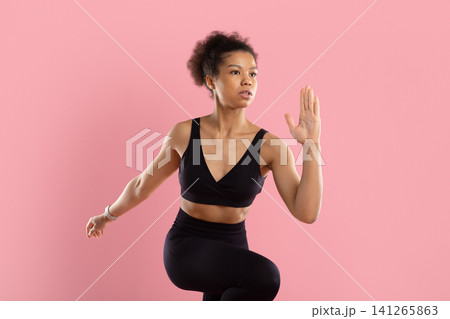 Focused young Black woman performing athletic running pose in activewear Focused young Black woman performing athletic running pose in activewear 141265863