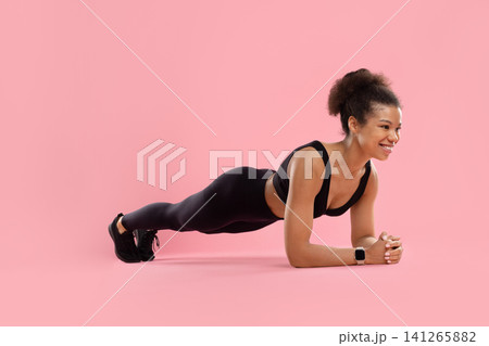 Smiling young Black female athlete in activewear performing forearm plank Smiling young Black female athlete in activewear performing forearm plank 141265882