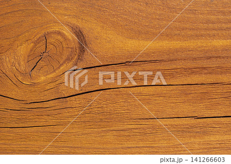 Horizontal close up of a rustic warm orange brown wood plank texture with a prominent round knot and deep horizontal cracks on a weathered timber surface 141266603