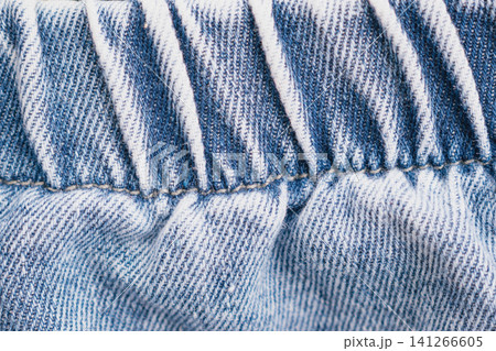 Horizontal macro close up shot of a blue jeans denim waistband with elastic band stretching and white vertical stitching details on classic casual pants Horizontal macro close up shot of a blue jeans denim waistband with elastic band stretching and white vertical stitching details on classic casual pants 141266605