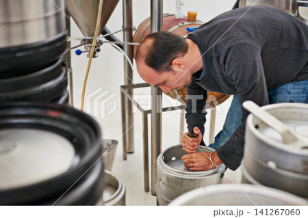 Brewery, man and kegs machine with manufacturing for craft beer, alcohol and production process in factory. Industrial industry, worker and working in distillery with tank for brewing in warehouse 141267060