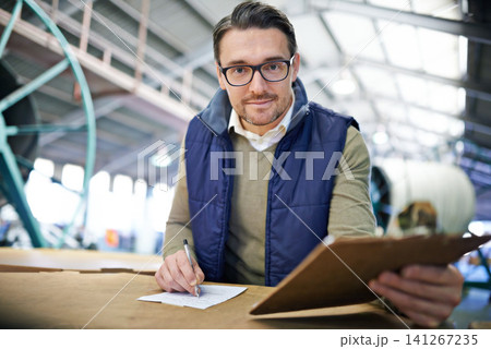 Man, manager and writing with clipboard in logistics at factory with machines for supply chain. Portrait, warehouse and paperwork on table at manufacturing and distribution business with smile 141267235