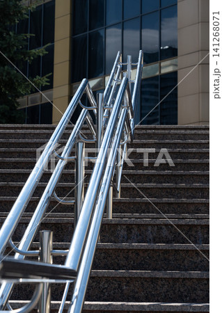 A Close-Up View of Modern Stainless Steel Handrails Along Stairs Leading Up to a Tall Glass Building Under Clear Blue Skies A Close-Up View of Modern Stainless Steel Handrails Along Stairs Leading Up to a Tall Glass Building Under Clear Blue Skies 141268071