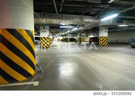Dimly Lit Parking Garage with Yellow and Black Warning Stripes on Columns and Parked Vehicles Amidst an Open Space 141268092