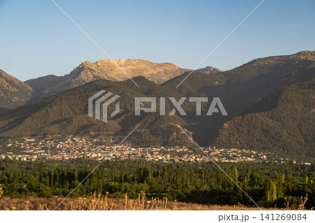 Golden sunlight casts a warm glow over a town surrounded by majestic mountains, showcasing natures beauty at dusk with clear skies. Golden sunlight casts a warm glow over a town surrounded by majestic mountains, showcasing natures beauty at dusk with clear skies. 141269084