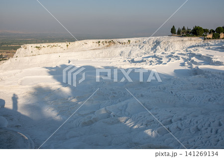 Travelers admire the breathtaking white travertine terraces of Pamukkale, formed by mineral-rich thermal waters, during the early morning light. 141269134