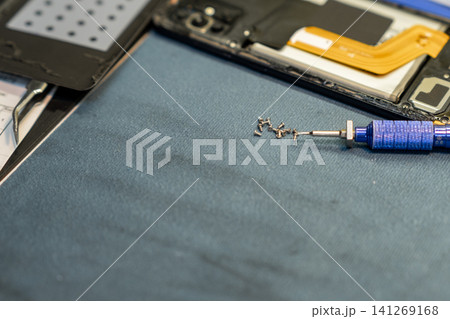 Screws and tools are organized neatly on a work surface while a technician focuses on the intricate details of phone repair in a shop. Screws and tools are organized neatly on a work surface while a technician focuses on the intricate details of phone repair in a shop. 141269168