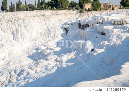 Visitors explore the stunning white travertine terraces of Pamukkale, known for their thermal waters and breathtaking landscapes, on a bright sunny day. Visitors explore the stunning white travertine terraces of Pamukkale, known for their thermal waters and breathtaking landscapes, on a bright sunny day. 141269179