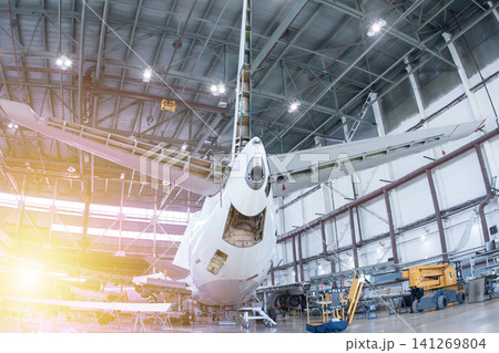 Rear view of white passenger airplane in the aircraft hangar. Plane under maintenance. Checking mechanical systems for flight operations Rear view of white passenger airplane in the aircraft hangar. Plane under maintenance. Checking mechanical systems for flight operations 141269804