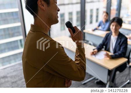 マイクを持って講義する男性講師と受講者たち マイクを持って講義する男性講師と受講者たち 141270226