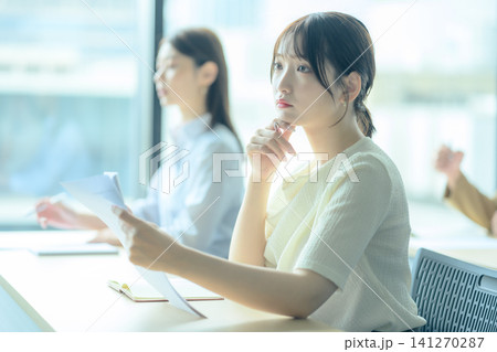 会議で資料を見ながら考える若い女性 会議で資料を見ながら考える若い女性 141270287