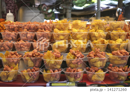 Assortment of fried snacks and sausages displayed in clear plastic cups at a market stall Assortment of fried snacks and sausages displayed in clear plastic cups at a market stall 141271260