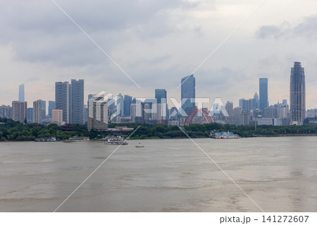 Wuhan city skyline along a wide river featuring a red arch bridge 141272607