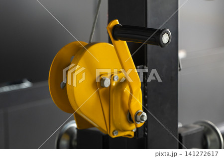 Close-up of a yellow hand winch pulley with a black crank handle 141272617