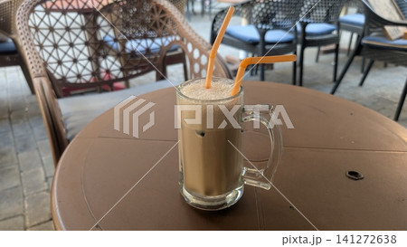 An iced cafe latte with foam, served in a large glass with two orange straws, sitting on an outdoor cafe table An iced cafe latte with foam, served in a large glass with two orange straws, sitting on an outdoor cafe table 141272638