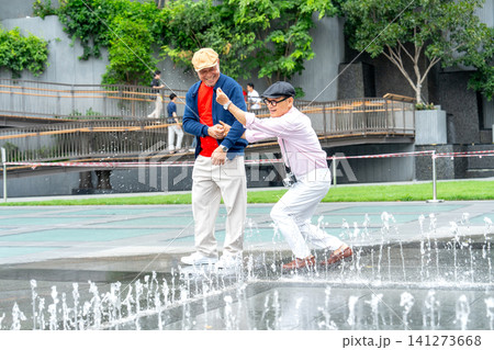 Couple Asian senior lgbtq men enjoy to play with fountain in the public park together and happiness during relax in the big city. Couple Asian senior lgbtq men enjoy to play with fountain in the public park together and happiness during relax in the big city. 141273668