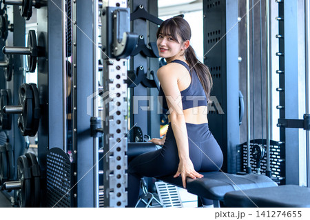 仕事帰りにジムに通う若い女性　パワーラックに座って笑顔で振り返る女性　トリミングアップ 141274655