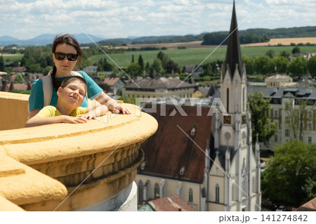 Happy mother and her young son enjoying panoramic city view from a historic balcony in summer Happy mother and her young son enjoying panoramic city view from a historic balcony in summer 141274842