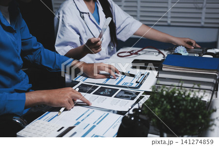 Two asian women doctors discuss meeting doctor's office medical clinic looking x-ray film consulting patient disease. Asian medical lab young women talking together discussing healthcare teamwork 141274859