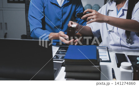 Two asian women doctors discuss meeting doctor's office medical clinic looking x-ray film consulting patient disease. Asian medical lab young women talking together discussing healthcare teamwork 141274860