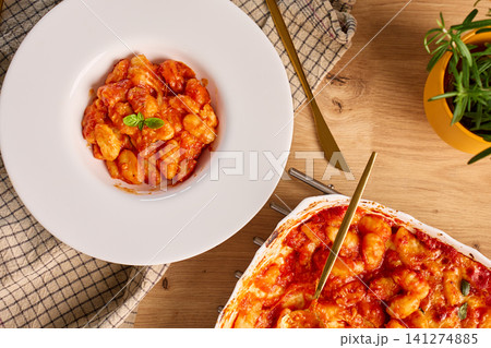 Gnocchi with tomato sauce, melted cheese and basil served on plate beside ceramic baking dish Gnocchi with tomato sauce, melted cheese and basil served on plate beside ceramic baking dish 141274885