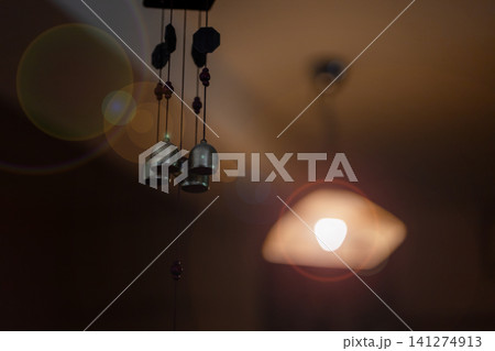 Dim interior room with hanging ceiling lamp casting warm amber glow, shadowed ceiling fixture, soft flare, textured surface, cozy domestic mood and quiet nighttime atmosphere Dim interior room with hanging ceiling lamp casting warm amber glow, shadowed ceiling fixture, soft flare, textured surface, cozy domestic mood and quiet nighttime atmosphere 141274913