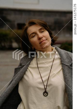 Woman enjoying the outdoors wearing a gray coat and necklace in a public area Woman enjoying the outdoors wearing a gray coat and necklace in a public area 141275176