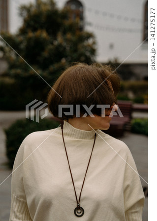 Woman with short hair turns away in a park wearing a sweater and necklace during a cloudy day Woman with short hair turns away in a park wearing a sweater and necklace during a cloudy day 141275177