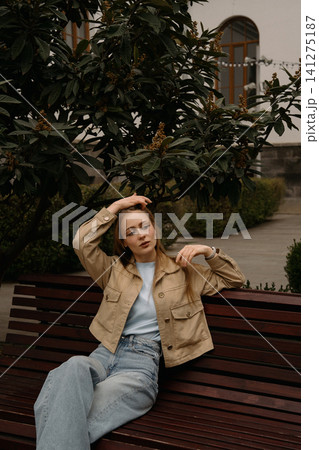 Girl with freckles sitting on bench in garden during sunny day with trees and plants around 141275187