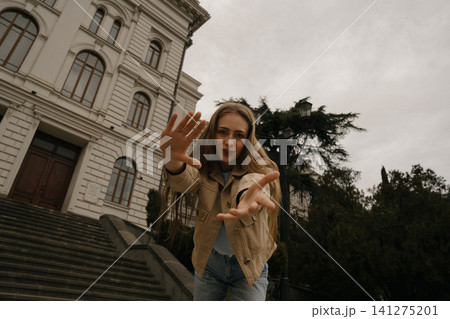 Girl with freckles reaches out near a historic building on a cloudy day in the city Girl with freckles reaches out near a historic building on a cloudy day in the city 141275201