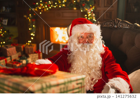 Merry Christmas. Santa Claus giving you present gift box in festive living room with fireplace decorations Christmas tree. Santa packing wrapping gift box on Christmas eve. Winter Holiday Celebrations Merry Christmas. Santa Claus giving you present gift box in festive living room with fireplace decorations Christmas tree. Santa packing wrapping gift box on Christmas eve. Winter Holiday Celebrations 141275632