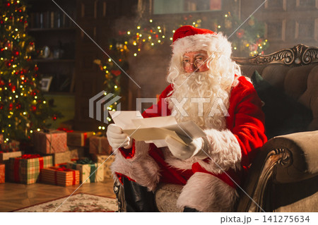 Merry Christmas. Happy Santa Claus reading letters from children in festive Christmas living room. Santa with xmas wish list letter on Christmas eve. Mail of Santa Claus. Winter Holiday Celebrations Merry Christmas. Happy Santa Claus reading letters from children in festive Christmas living room. Santa with xmas wish list letter on Christmas eve. Mail of Santa Claus. Winter Holiday Celebrations 141275634