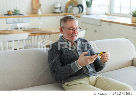 Senior man shopping online holding smartphone paying with credit card. Old grandfather buying on Internet enter credit card details. Online shopping delivery service Older generation modern tech usage Senior man shopping online holding smartphone paying with credit card. Old grandfather buying on Internet enter credit card details. Online shopping delivery service Older generation modern tech usage 141275683