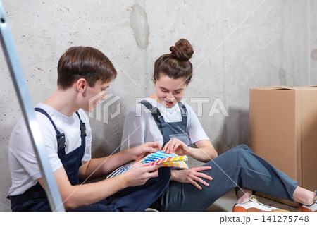 House decoration DIY renovation concept. Happy couple sitting on floor in empty room of new home planning design. Husband and wife holding swatch palette choosing colors for painting wall in new house House decoration DIY renovation concept. Happy couple sitting on floor in empty room of new home planning design. Husband and wife holding swatch palette choosing colors for painting wall in new house 141275748