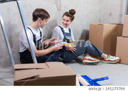 House decoration DIY renovation concept. Happy couple sitting on floor in empty room of new home planning design. Husband and wife holding swatch palette choosing colors for painting wall in new house House decoration DIY renovation concept. Happy couple sitting on floor in empty room of new home planning design. Husband and wife holding swatch palette choosing colors for painting wall in new house 141275764