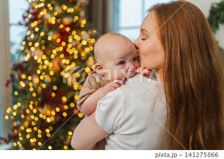 Merry Christmas Xmas. Happy family mother newborn baby child hugging bonding near Christmas tree at home. Mom girl kid celebrating Christmas New Year enjoying winter holidays together. Family moments Merry Christmas Xmas. Happy family mother newborn baby child hugging bonding near Christmas tree at home. Mom girl kid celebrating Christmas New Year enjoying winter holidays together. Family moments 141275866