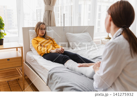 Girl with broken leg and doctor in clinic. Traumatologist orthopedist examines child leg in medical office. Doctor examining girl with medical plaster leg cast after broken ankle injury Rehabilitation Girl with broken leg and doctor in clinic. Traumatologist orthopedist examines child leg in medical office. Doctor examining girl with medical plaster leg cast after broken ankle injury Rehabilitation 141275932