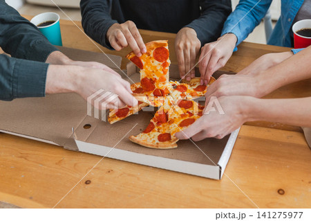 Home party. Top view male female hands taking slices of pizza from food delivery open box. Group of hungry friends sharing delicious lunch eating ordered pepperoni pizza. Food pizza delivery Home party. Top view male female hands taking slices of pizza from food delivery open box. Group of hungry friends sharing delicious lunch eating ordered pepperoni pizza. Food pizza delivery 141275977