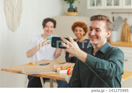 Cheers Funky mood. Happy group of friends make selfie. Man taking photo of friends at party. Group of multiracial young people taking photo on phone. Young people enjoy their company smile have fun 141275995
