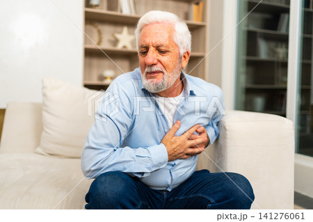 Pain on heart, heart attack. Unhappy middle aged senior man suffering from chest pain heart attack problems with health at home. Mature old senior grandfather touching chest experiencing infarction 141276061
