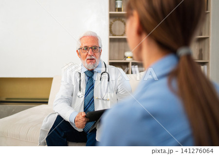 Senior man doctor examining young woman in doctor office clinic or at home. Girl patient and doctor have consultation in hospital room. Medicine healthcare medical checkup. Visit to doctor 141276064