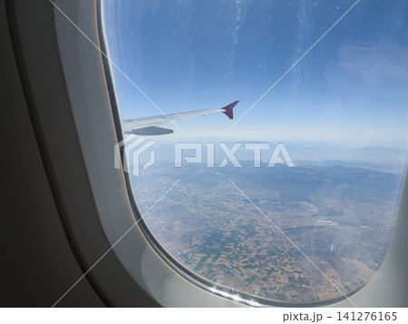 Airplane window. View of sky from inside of airplane. Airplane wing and sky clouds earth view. Blue clear sky and wings of plane window view. Tourism travel journey trip Airplane window. View of sky from inside of airplane. Airplane wing and sky clouds earth view. Blue clear sky and wings of plane window view. Tourism travel journey trip 141276165
