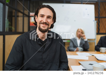 Portrait of team leader businessman in office, colleagues meeting in background. Confident business leader man sitting in office. Boss leader professional worker. Working process office life career Portrait of team leader businessman in office, colleagues meeting in background. Confident business leader man sitting in office. Boss leader professional worker. Working process office life career 141276236