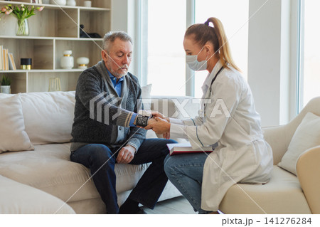 Female doctor senior man taking his blood pressure in doctor office or at home. Old man patient and doctor have consultation in hospital room. Medicine healthcare medical checkup. Visit to doctor Female doctor senior man taking his blood pressure in doctor office or at home. Old man patient and doctor have consultation in hospital room. Medicine healthcare medical checkup. Visit to doctor 141276284
