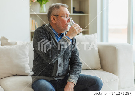 Senior man holding glass drinking fresh water at home. Mature old senior thirsty grandfather takes care of his health. Healthcare water balance. Elderly healthy lifestyle 141276287