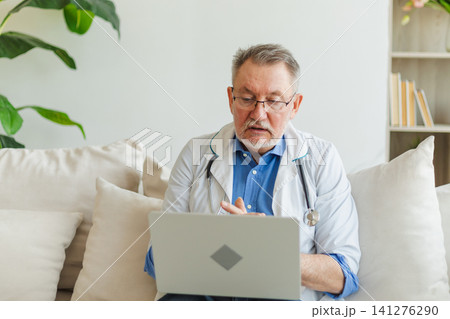 Senior man doctor with laptop talk on video call have consultation with patient. Professional senior mature healthcare expert examining patient online. Medicine healthcare medical checkup Senior man doctor with laptop talk on video call have consultation with patient. Professional senior mature healthcare expert examining patient online. Medicine healthcare medical checkup 141276290